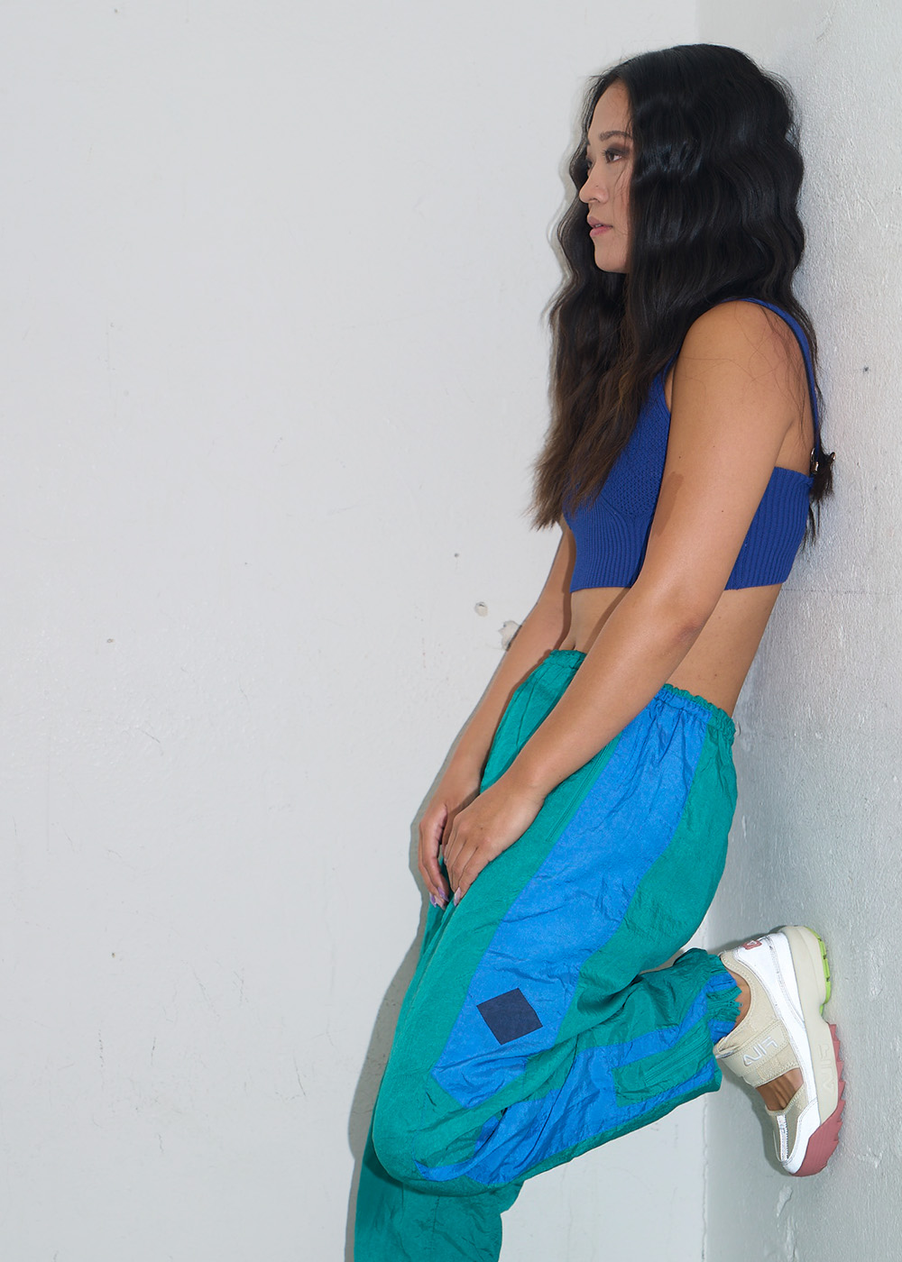 Kvinna iklädd retro sportkläder i starka färger lutar sig mot en vägg.