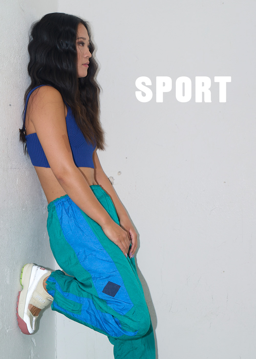 Kvinna i retro sport kläder står lutad mot en vägg. Gå till sportkläder.