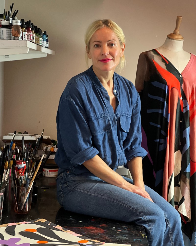 Stina Persson sitter på sitt arbetsbord bland penslar och färger.