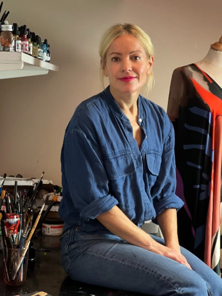Stina Persson sitter på sitt arbetsbord bland penslar och färger.