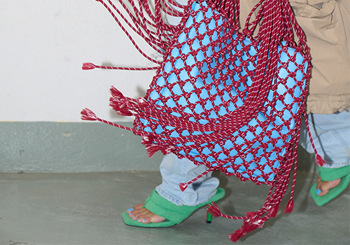 Woman wearing green sandals carries a braided red bag.